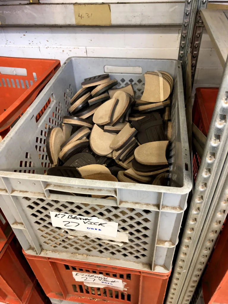 Grå låda fylld med klackdelar och suldelar
